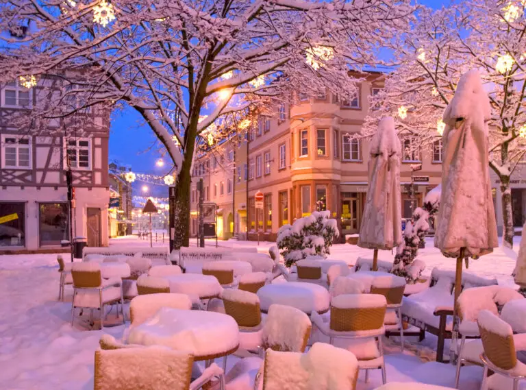Weihnachtsstimmung beim Café Cielo nach Neuschnee. Zu sehen sind schneebedeckte Tische und Stühle und mit Sternen beleuchtete Bäume.